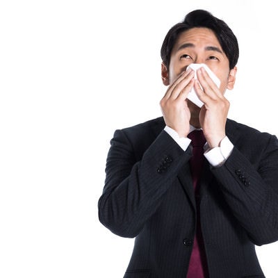 花粉症で鼻を押さえる会社員の写真