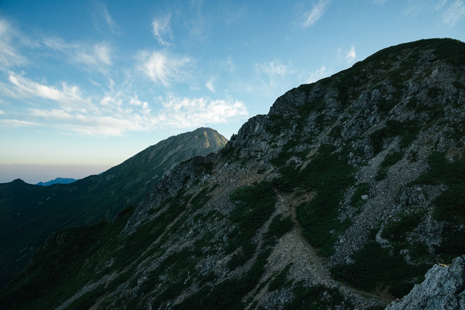 「岩稜の傾斜面から続く登山道」の写真