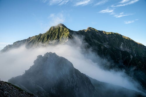 雲に隠れた岩稜と聳える稜線の写真