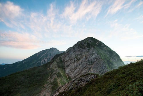 夕焼け色に染まる岩稜と登山道の写真