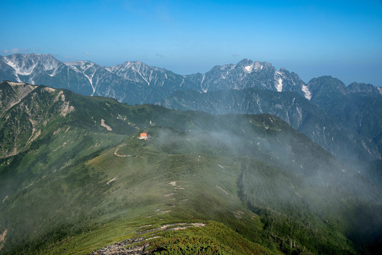 「登山道の先に見える山荘と連峰」の写真
