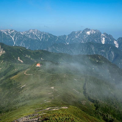登山道の先に見える山荘と連峰の写真