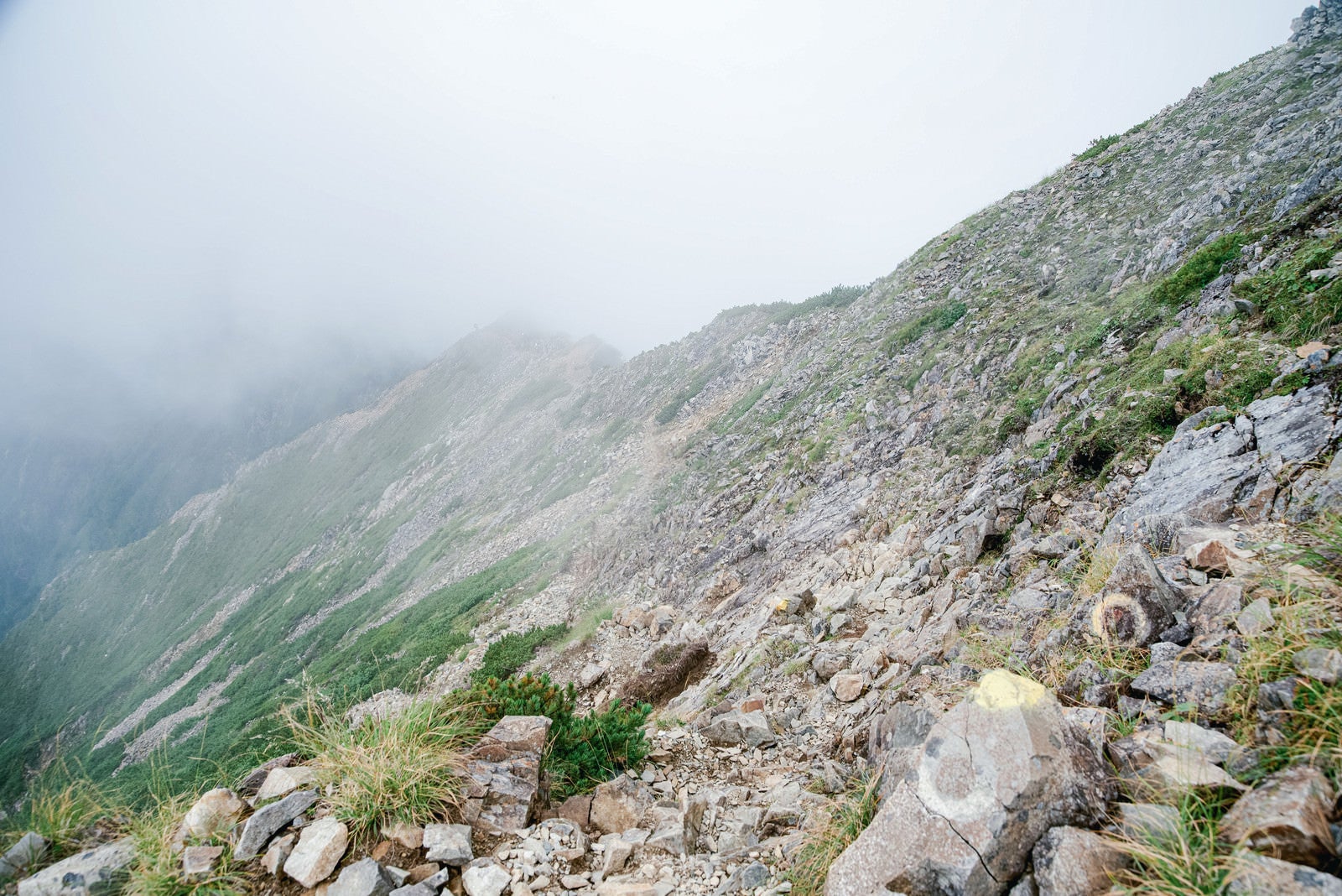 「雲に覆われるガレの続く登山道」の写真