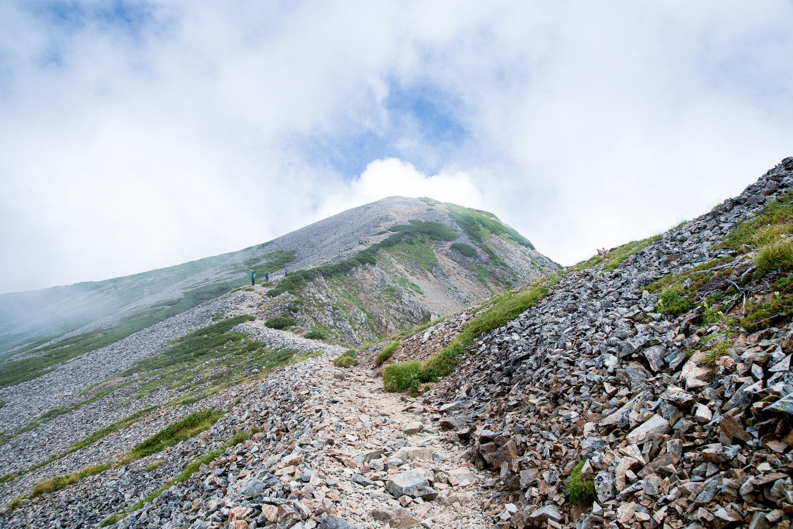 「沸き立つ雲の中へと続くガレの登山道」の写真