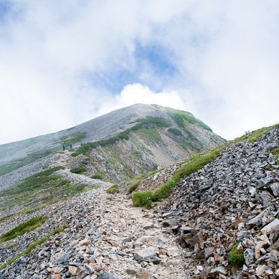 沸き立つ雲の中へと続くガレの登山道の写真