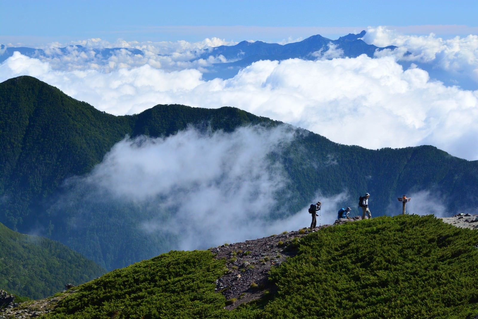 「山間の雲と登山道を歩く人」の写真