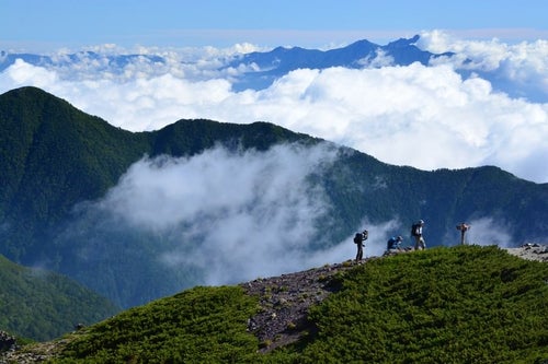 山間の雲と登山道を歩く人の写真