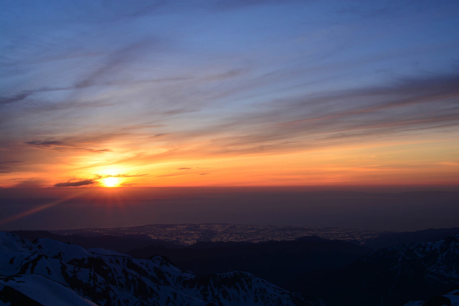 「残雪の山から見る日本海に沈む夕日」の写真