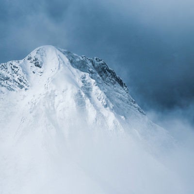 灰色の雲の切れ間から姿を出した阿弥陀岳（八ヶ岳南部）の写真