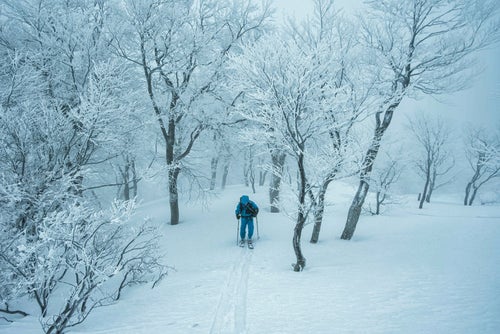 雪山のシュプールをなぞる登山者の写真