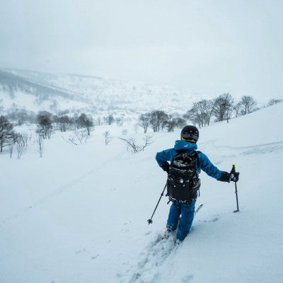 雪深い斜面を滑るスキーヤーの写真