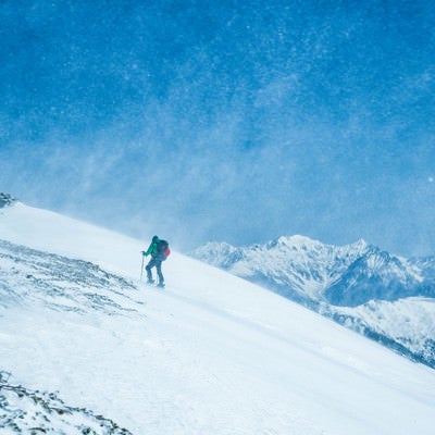 舞い上がる雪と山スキーヤーの写真
