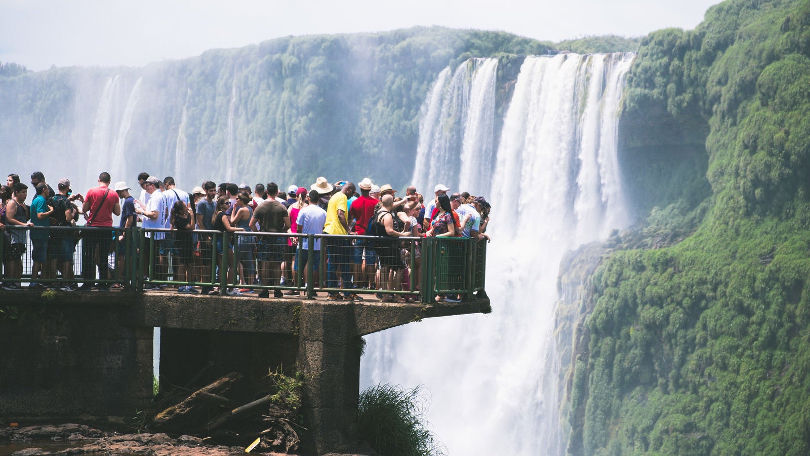 「絶景の滝の上に設置された遊歩道と下を覗き見る観光客（イグアスの滝）」の写真