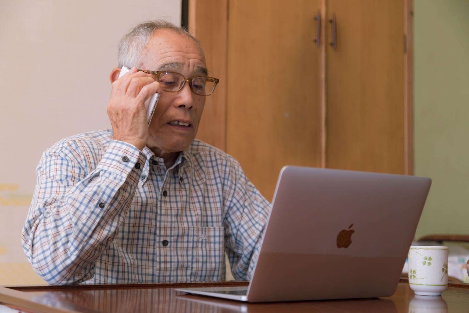 「パソコンの使い方を電話で確認しながら操作する高齢者男性」の写真［モデル：まーちゃん］