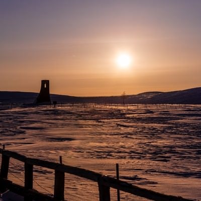 夕刻の雪原に立つ避難塔の写真