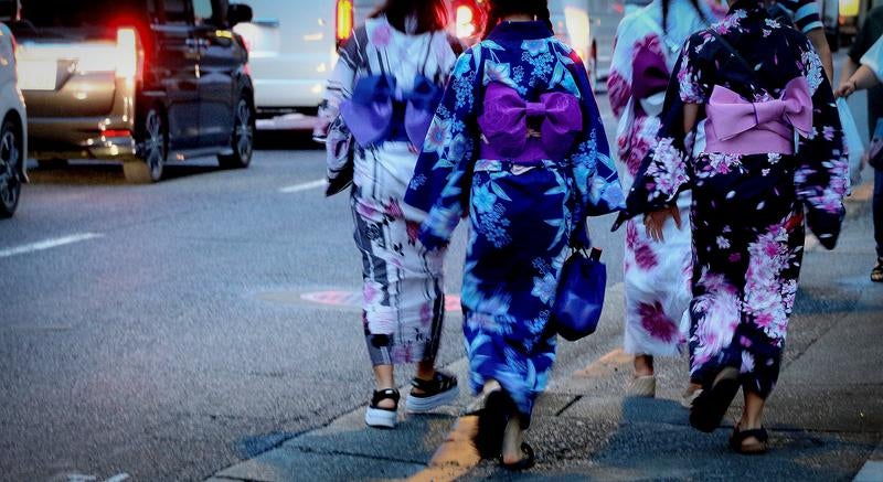 夏の夕暮れ、浴衣姿で街を歩く女性達の後ろ姿の写真