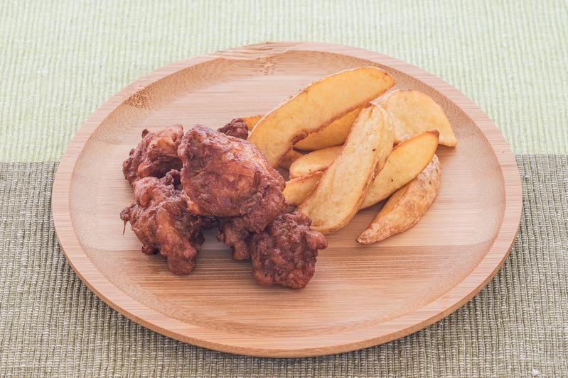 木製の丸皿に盛られた唐揚げとポテトフライの写真