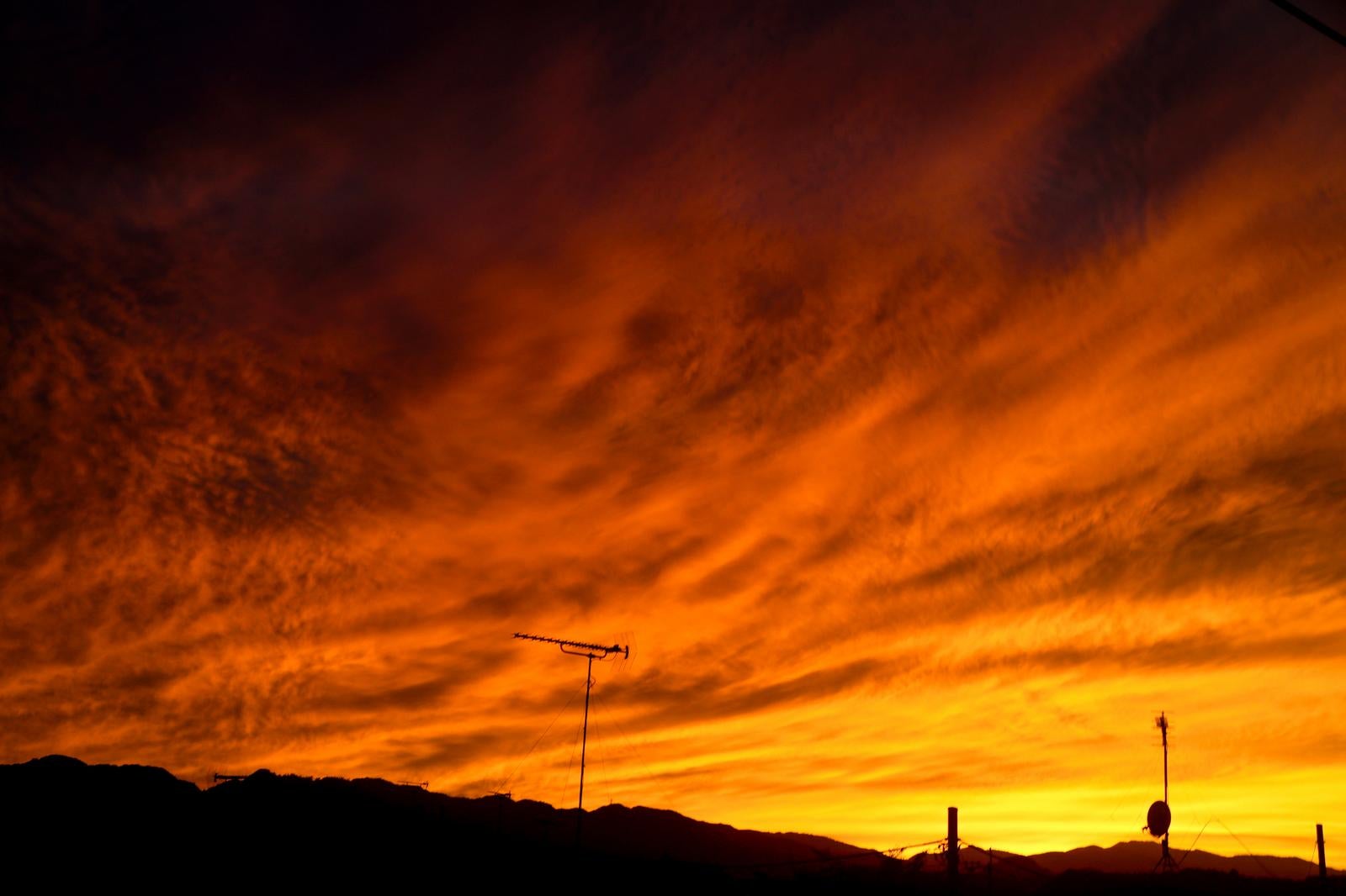 オレンジ色に輝く夕焼け空のなかで、丘の上に立つアンテナがシルエットになっている風景