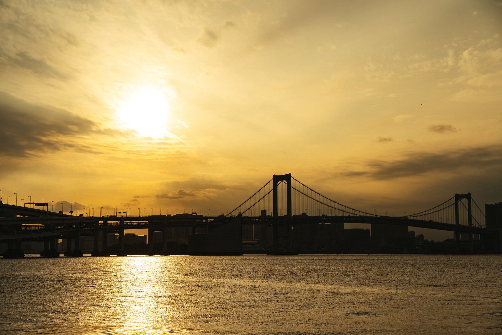 「夕日に照らされる海面と橋のシルエット」の写真