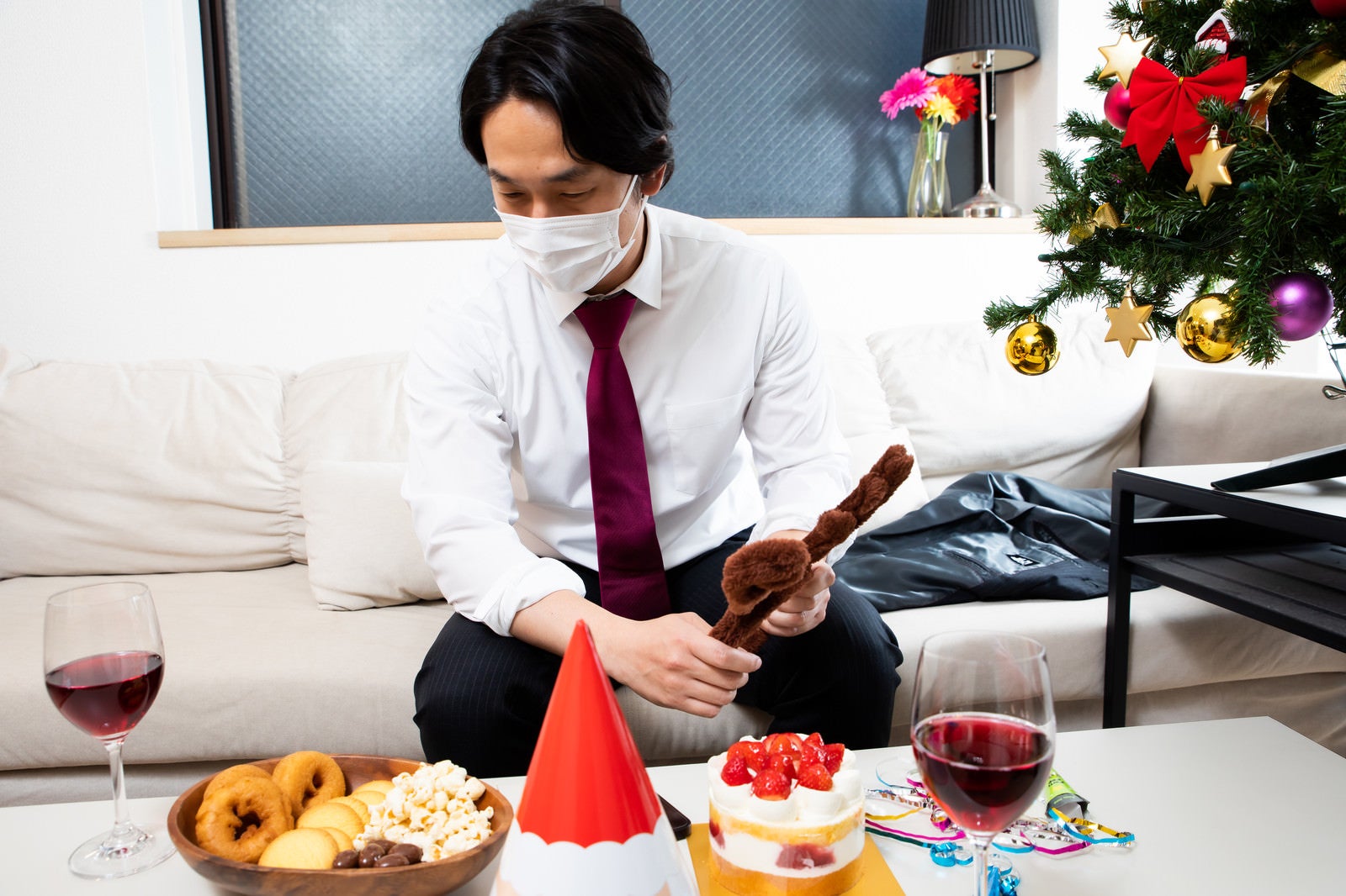 「机に並んだクリスマス用のパーティーフードとマスク着用の会社員」の写真［モデル：大川竜弥］
