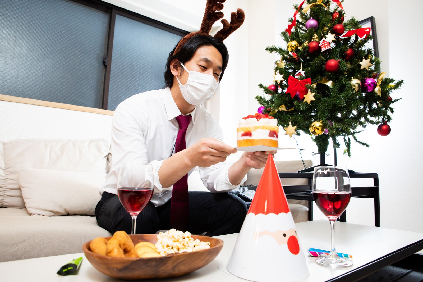「クリスマスケーキを見つめるマスク着用の会社員」の写真［モデル：大川竜弥］