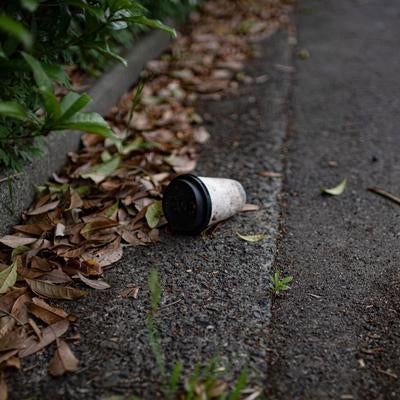 落ち葉が積もる歩道に無造作に捨てられている紙コップの写真