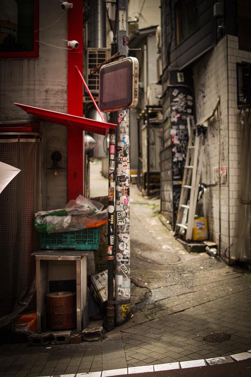ステッカーだらけの電柱と古びた看板が目を引く裏路地の写真