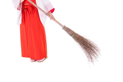 竹ほうきで掃き掃除をする巫女の足元の写真