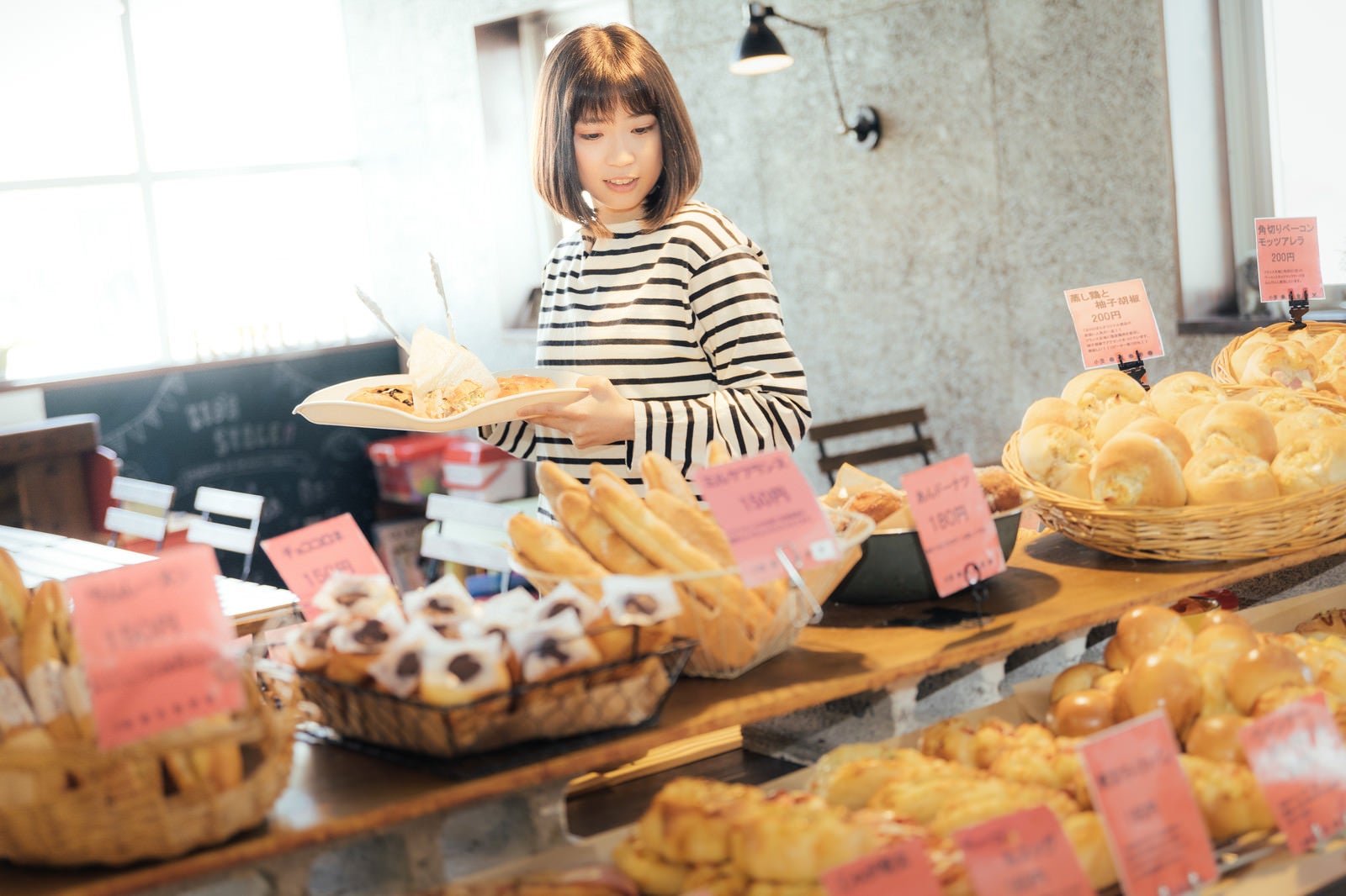 「手作りパンのお店でトレイを手に取り店内を歩く女性」の写真［モデル：塩田みう］