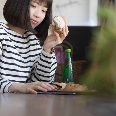 フードコートでパンを食べながらスマホを見る女性の写真