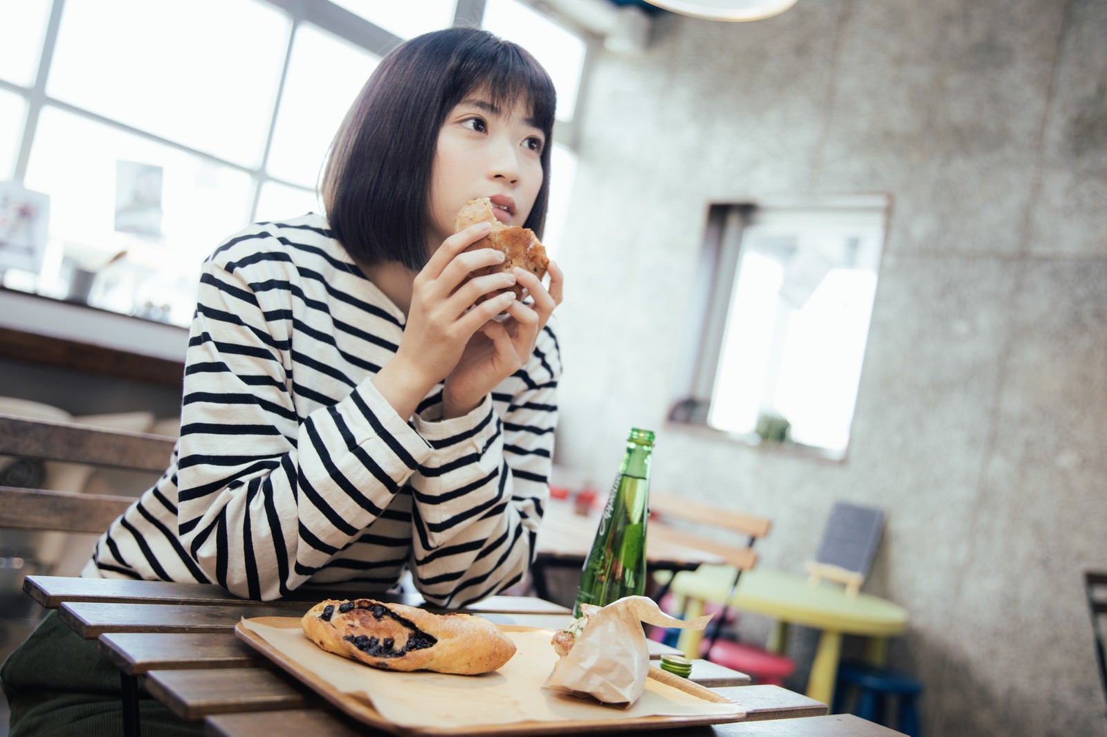 「フードコートでおやつに菓子パンを食べる女性」の写真［モデル：塩田みう］