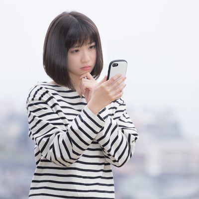 電波がなくてネットに繋がらないスマホを見つめる女性の写真