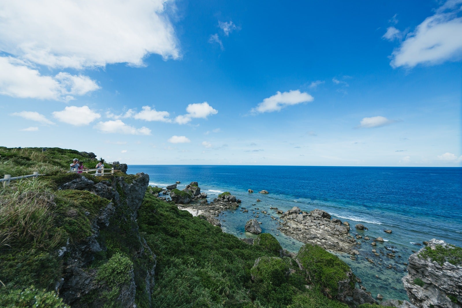 「緑豊かな崖の上から望む沖縄宮古島の美しい青い海と白い雲が浮かぶ夏空」の写真