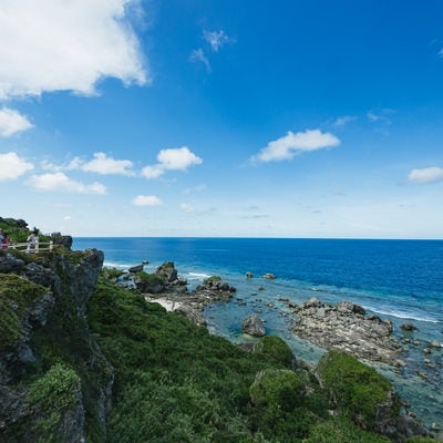 緑豊かな崖の上から望む沖縄宮古島の美しい青い海と白い雲が浮かぶ夏空の写真
