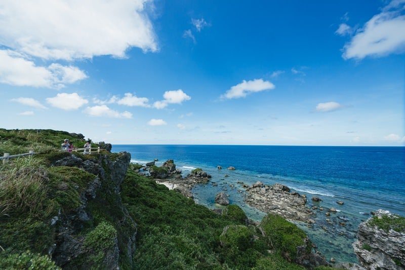 緑豊かな崖の上から望む沖縄宮古島の美しい青い海と白い雲が浮かぶ夏空の写真