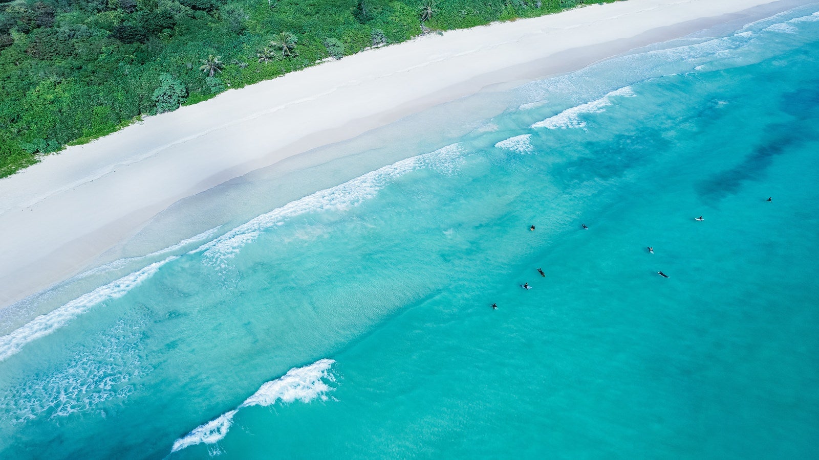 「白浜に寄せる波と波待ちするサーファー」の写真
