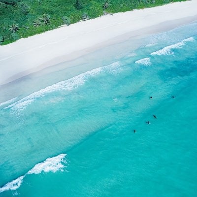 白浜に寄せる波と波待ちするサーファーの写真