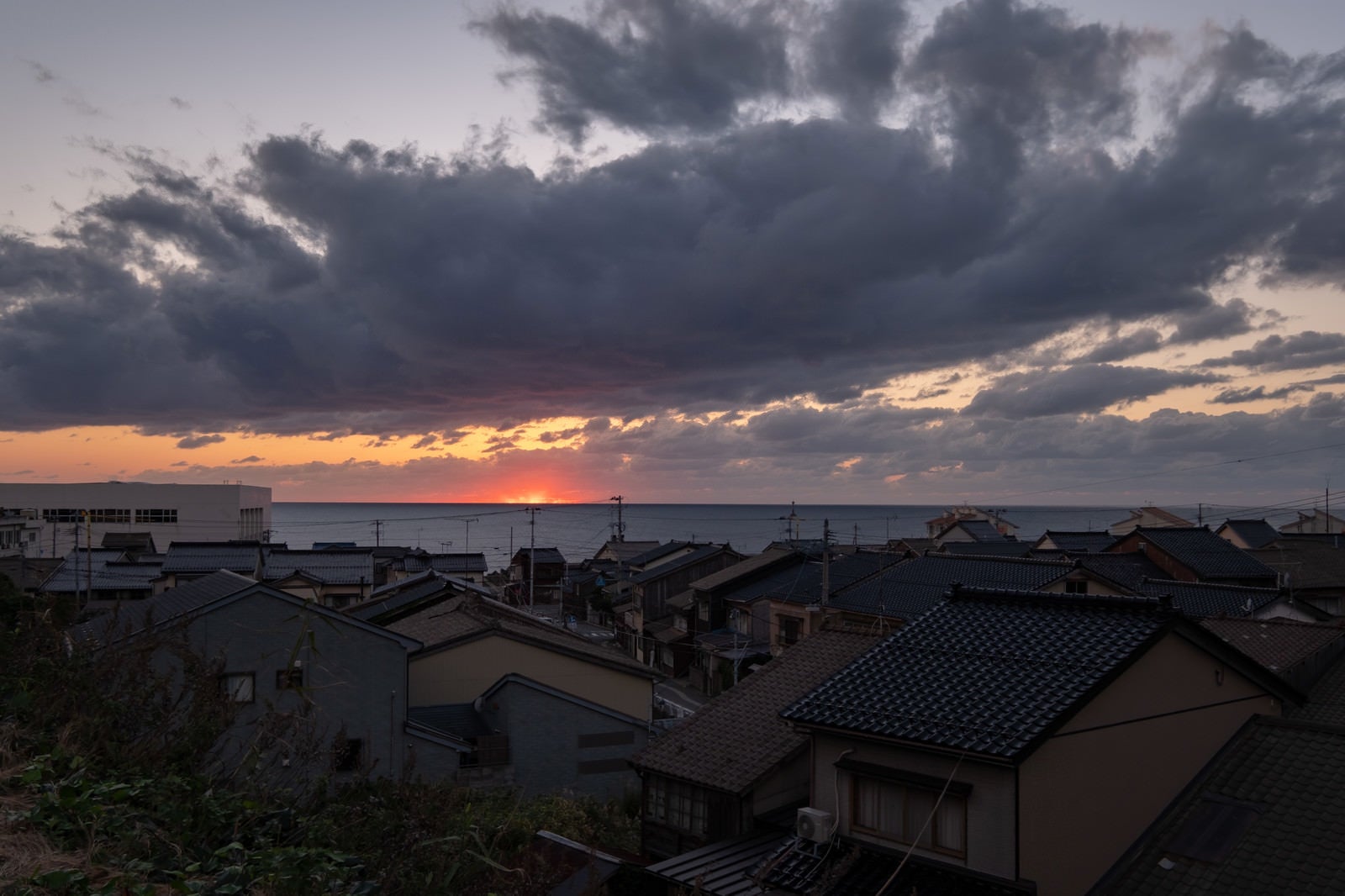 「沈む夕日と海沿いの民家」の写真