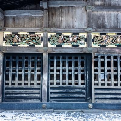 冬の日光東照宮で見る格子戸と上部の三猿の彫刻装飾と雪景色の写真