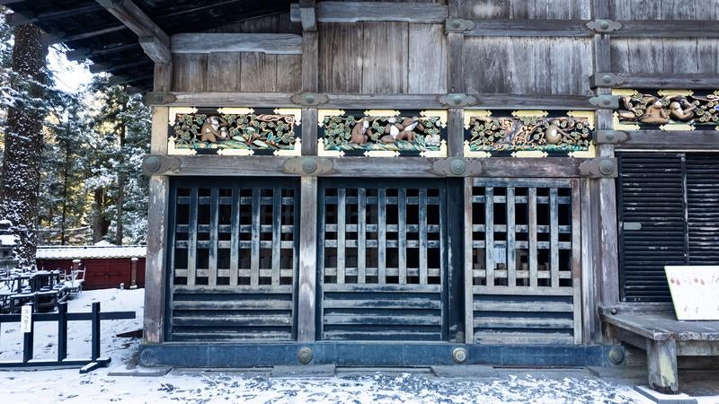 冬の日光東照宮で見る格子戸と上部の三猿の彫刻装飾と雪景色