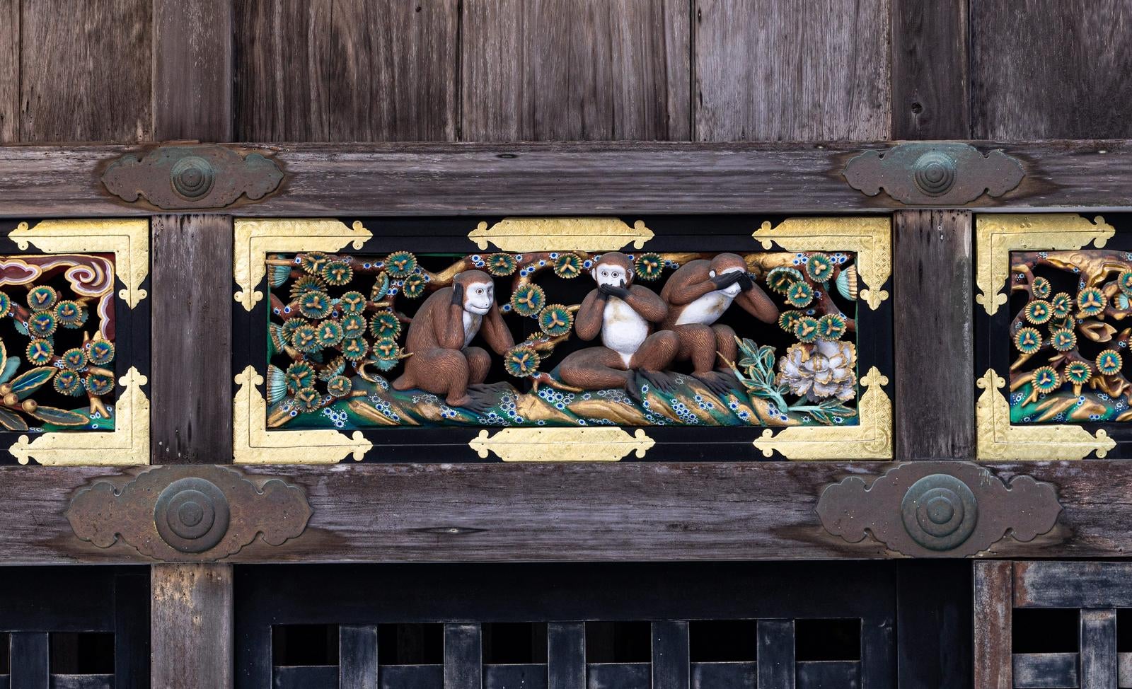黒い木製の建造物に金色枠で装飾された三匹の猿の浮彫り彫刻