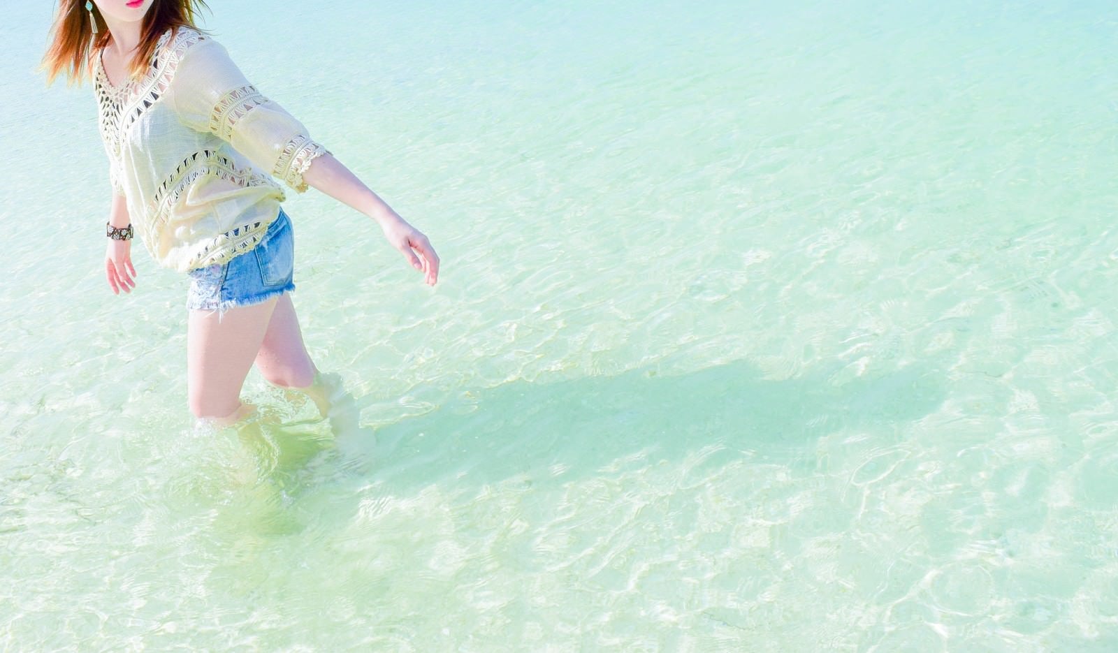 「穏やかな透明な海の浅瀬を歩く女性」の写真