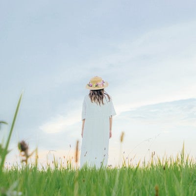 草原で立ちつくす麦わら帽子の女性の写真