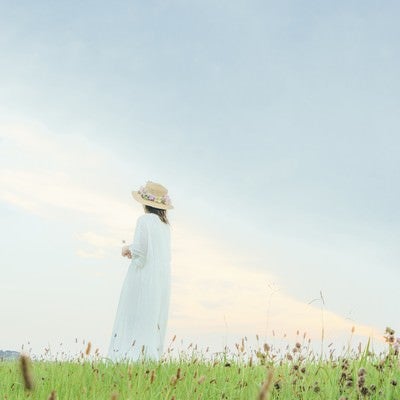 草原で遠くを見つめる女性の後ろ姿の写真