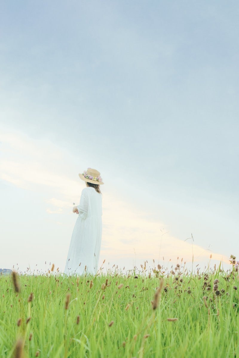 「草原で遠くを見つめる女性の後ろ姿」の写真