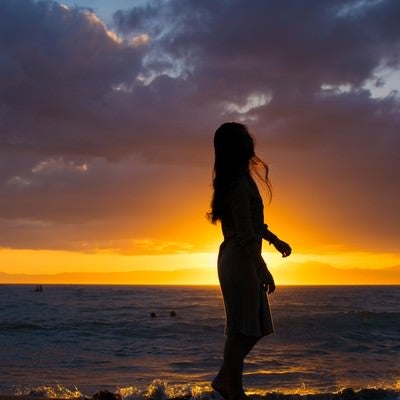 夕日に照らされる砂浜を歩く女性のシルエットの写真