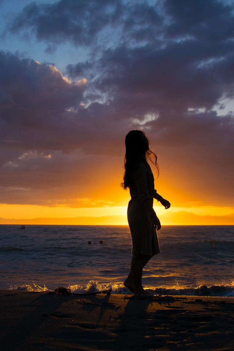 「夕日に照らされる砂浜を歩く女性のシルエット」の写真