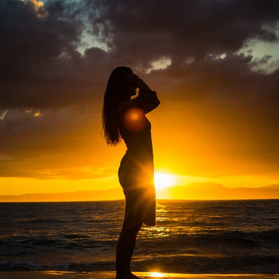 夕日のレイラインに立つ女性のシルエットの写真