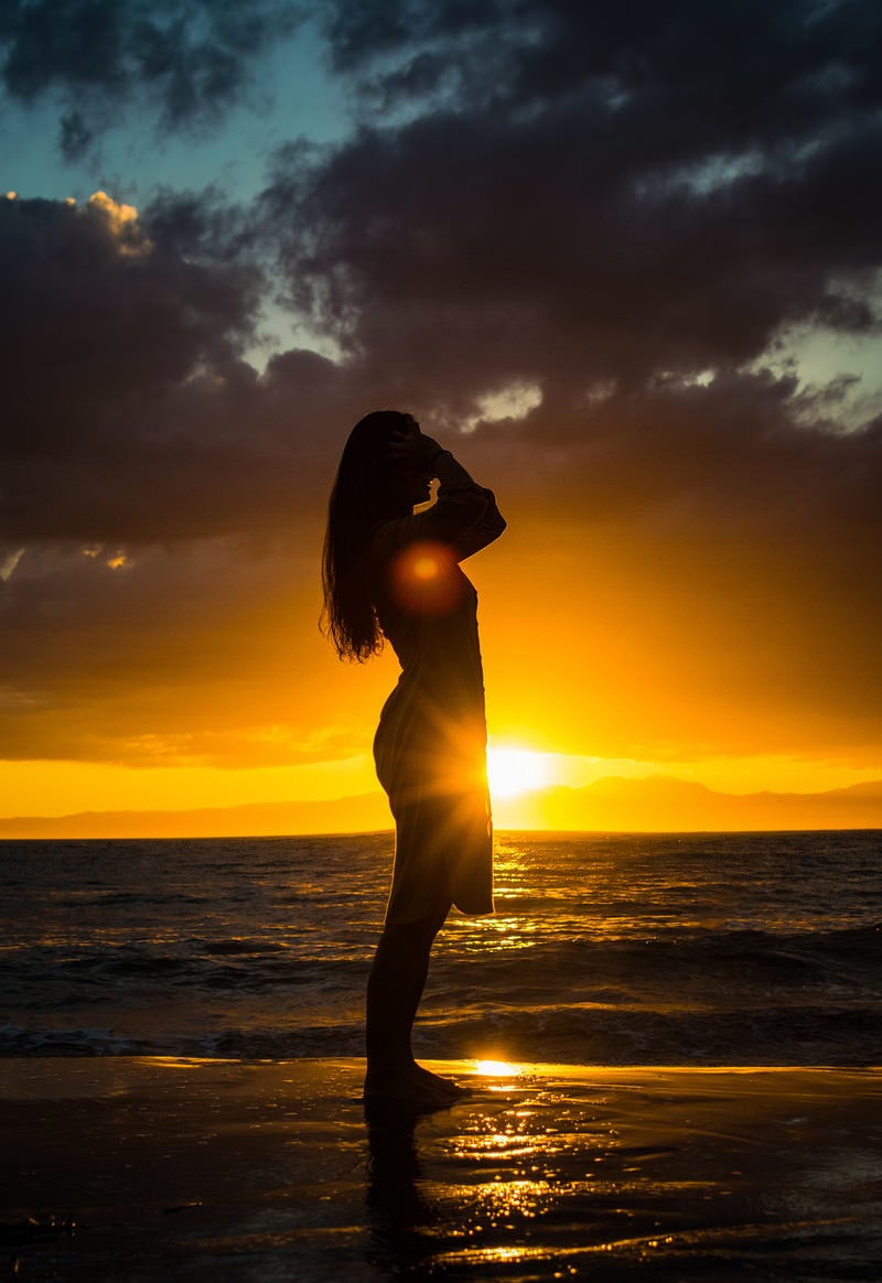「夕日のレイラインに立つ女性のシルエット」の写真