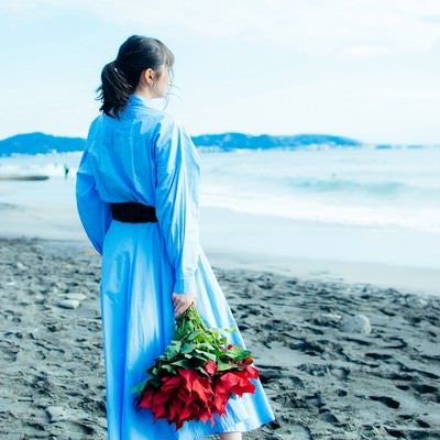 波打ち際で赤い花束を手にする女性の写真